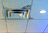 Water-stained ceiling tile around air conditioning duct with can light next to stain.