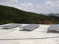 Photo of 3 photovoltaic arrays with hills and ocean in the background.