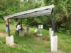 Photo of a photovoltaic array powering a water pump with jungle in the background.