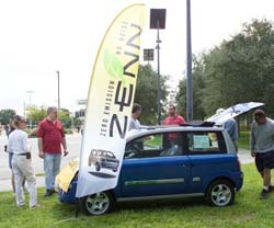 Photo of people looking at the Zenn car - zero emissions and no noise.